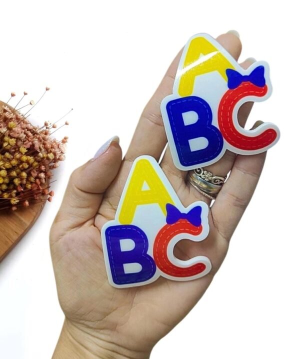 APLIQUE EM ACRÍLICO CURVADO ABC C/ LAÇO 7CM UND